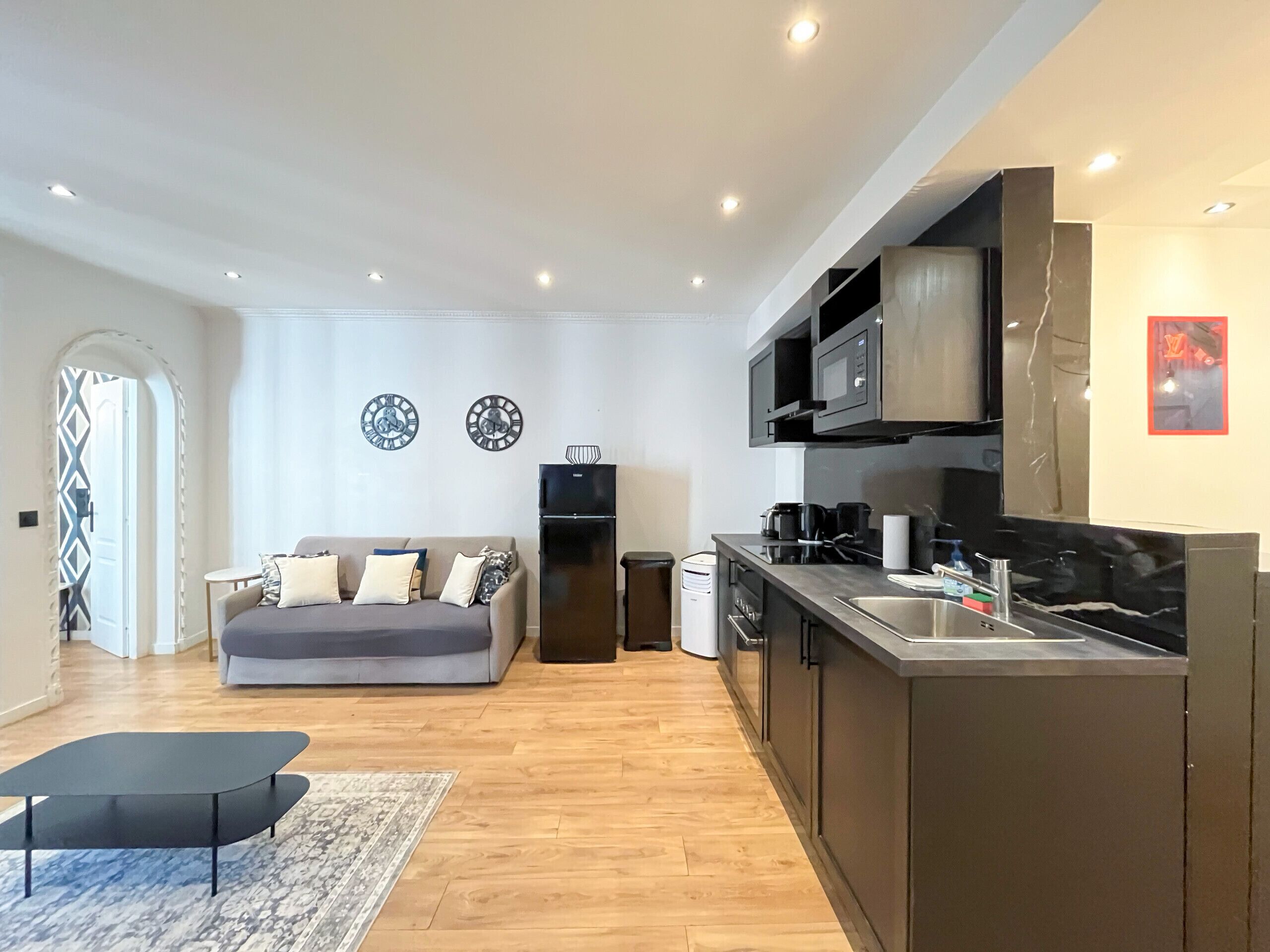 A modern living room with a sofa, a coffee table, and a kitchen area with a sink and microwave.