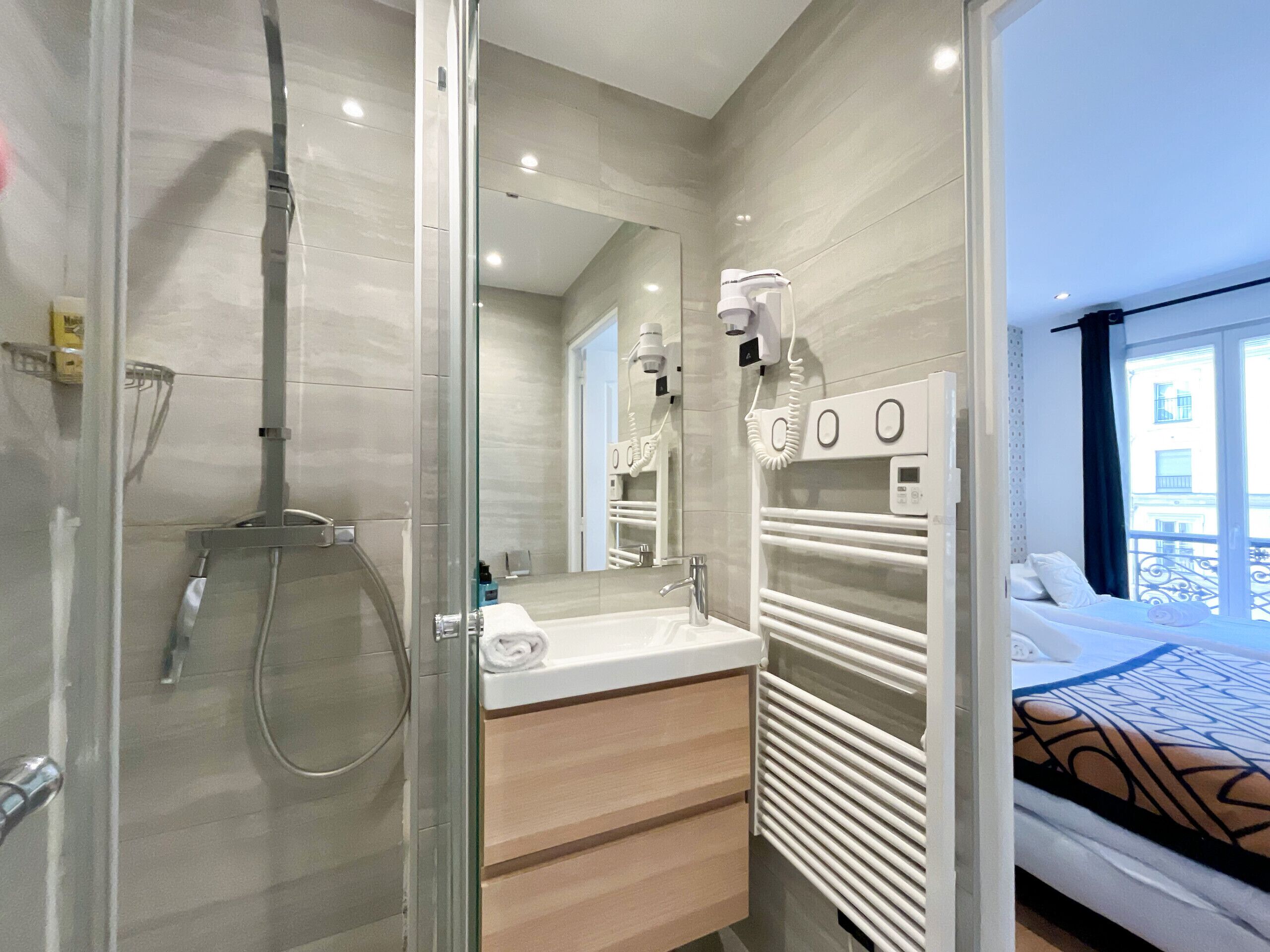 A modern bathroom with a glass shower enclosure, a vanity with a mirror, and a bed with a patterned bedspread.