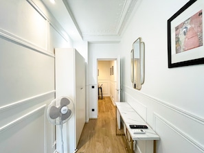 A hallway with a white fan, a framed picture, and a table with a remote control.