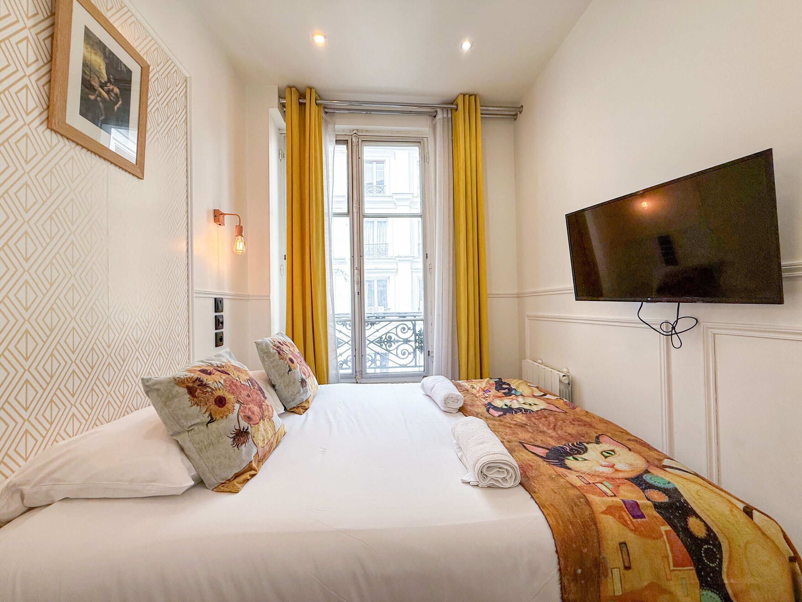 Una habitació d'hotel amb un llit, televisió, finestra amb cortines grogues i un mur amb disseny.