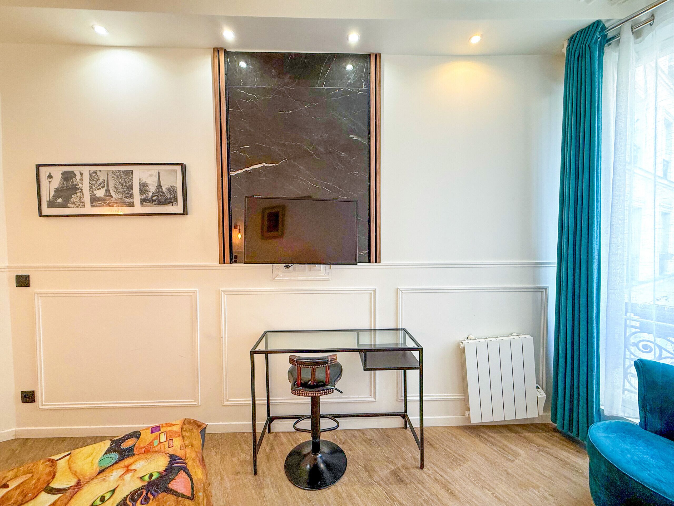 Una habitación con ventana enmarcada en mármol, una mesa de cristal con una silla, un radiador y un sofá azul.
