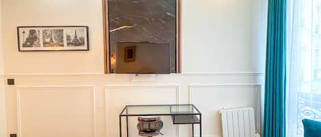 A room with a marble-framed window, a glass table with a chair, a radiator, and a blue sofa.