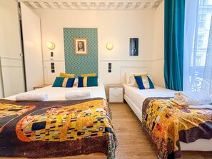 Ein Hotelzimmer mit zwei Betten, jedes mit gemusterten Bettbezügen und einem gerahmten Kunstwerk darüber.
