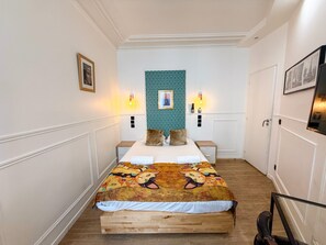 A bedroom with a wooden bed, two bedside tables, a patterned wall, and a framed picture on the wall.