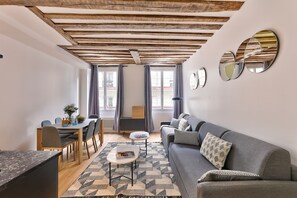 A modern living room with a wooden ceiling, a grey sofa, a dining table with chairs, and a small coffee table. - 96 - Urban Musée Grévin (París)