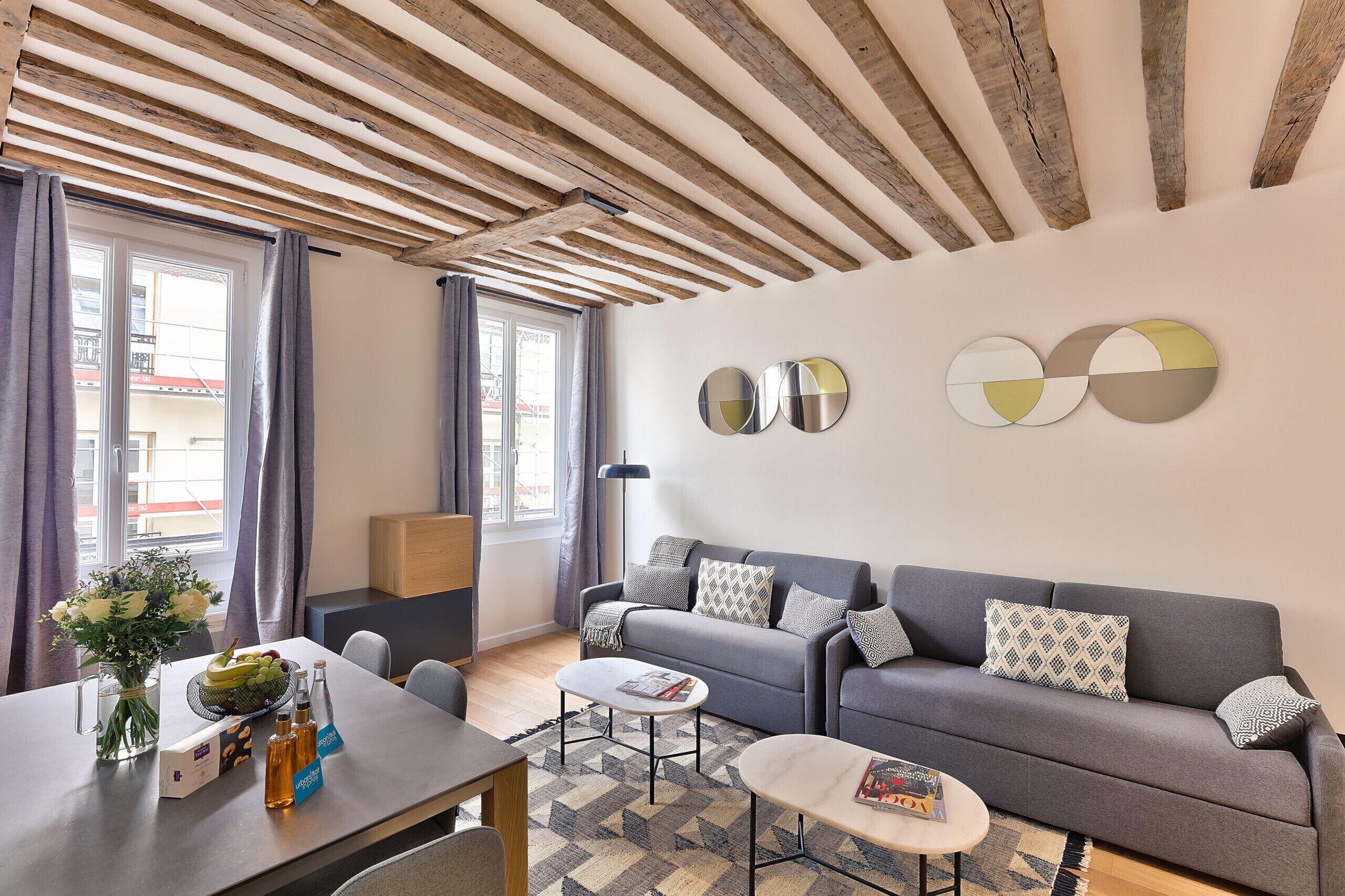 A modern living room with a grey sofa, a coffee table, and a dining area with a table set for two.