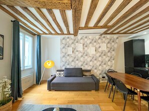 Un salon moderne avec un plafond en bois, un canapé gris, une table à manger avec des chaises et un mur à motifs.