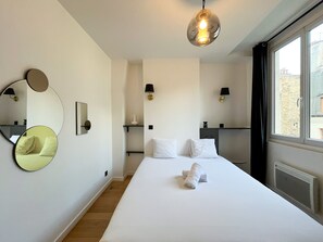 A hotel room with a large bed, two bedside tables, a mirror, and a hanging light fixture.