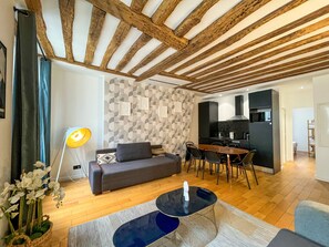 Un salon moderne avec un canapé, une table basse et un coin repas comprenant une table et des chaises. On aperçoit une cuisine au fond.