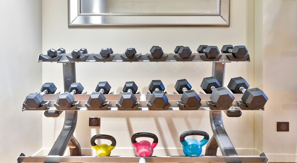 A wall-mounted dumbbell rack with multiple sets of hexagonal dumbbells and kettlebells.