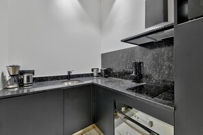 A modern kitchen with dark cabinetry, a black countertop, and stainless steel appliances.