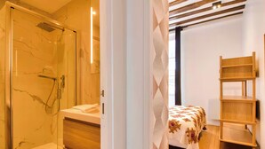 Un baño moderno con ducha de vidrio, tocador de madera y cama con colcha estampada.