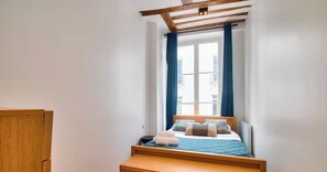 Une chambre à coucher avec un lit, une tête de lit en bois, une fenêtre avec des rideaux et une poutre en bois au plafond.