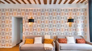 Une pièce moderne avec deux canapés, un papier peint à motifs géométriques et des luminaires fixés au mur.