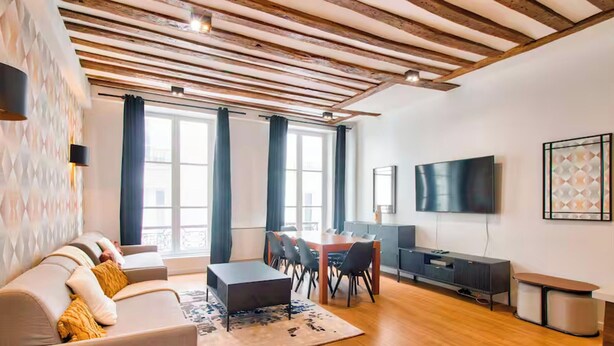 Una sala moderna con techo de madera, un sofá, una mesa de centro, un televisor y un comedor.