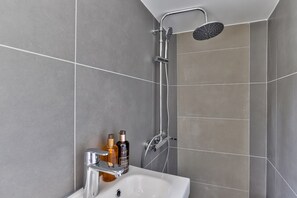 Un baño moderno con ducha, lavamanos y dos botellas de jabón líquido.