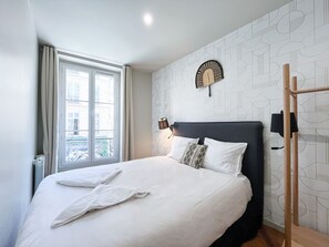 A neatly made bed with white linens and pillows, a bedside lamp, and a patterned wall.