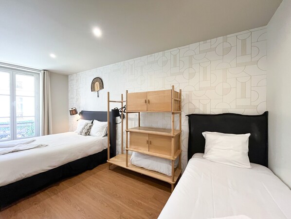A hotel room with two beds, a wooden bunk bed, a patterned wall, and a window with a view.