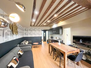A modern living room with a sofa, a wooden dining table, and a TV.