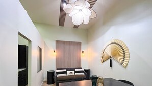 Un espace repas moderne avec une table sombre, deux chaises, un ventilateur fixé au mur et un panneau décoratif orné de lignes verticales.