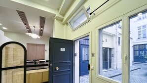 L’entrée d’un hôtel, avec une porte bleu foncé, un espace de réception doté d’un comptoir, et une vue sur la rue.