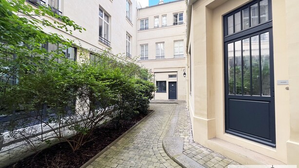 Une ruelle étroite avec un chemin pavé, bordée de bâtiments dotés de nombreuses fenêtres et d’une porte.