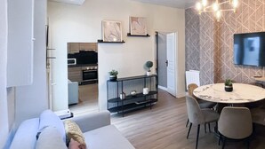 A modern living room with a sofa, a dining table with chairs, a kitchen in the background, and a patterned wall. - Urban Flat 06 - Charming 2 BDR in Paris (París)