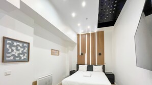 A modern hotel room with a bed, a wall-mounted artwork, a small bedside table, and a radiator.