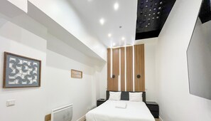 Una habitación de hotel moderna con una cama, una obra de arte colgada en la pared, una mesita de noche pequeña y un radiador.