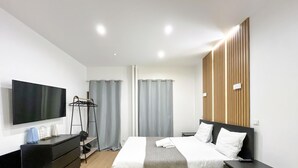 Una habitación de hotel moderna con cama, mesitas de noche, televisor, armario y ventana con cortinas.