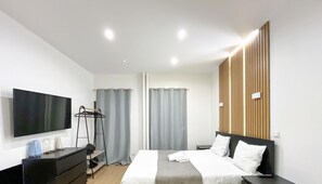 Quarto de hotel moderno com cama, mesas de cabeceira, televisão, guarda-roupa e janela com cortinas.