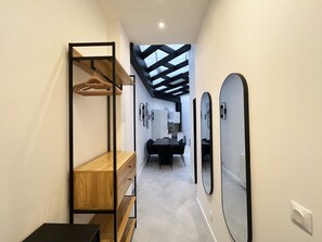 A modern hallway with a wooden shelf unit, a black chair, and a dining table in the background.
