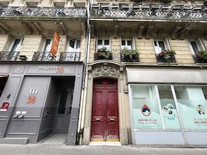 A hotel facade with a prominent red door, a balcony with plants, and a sign for 'magenta hotel 38'.