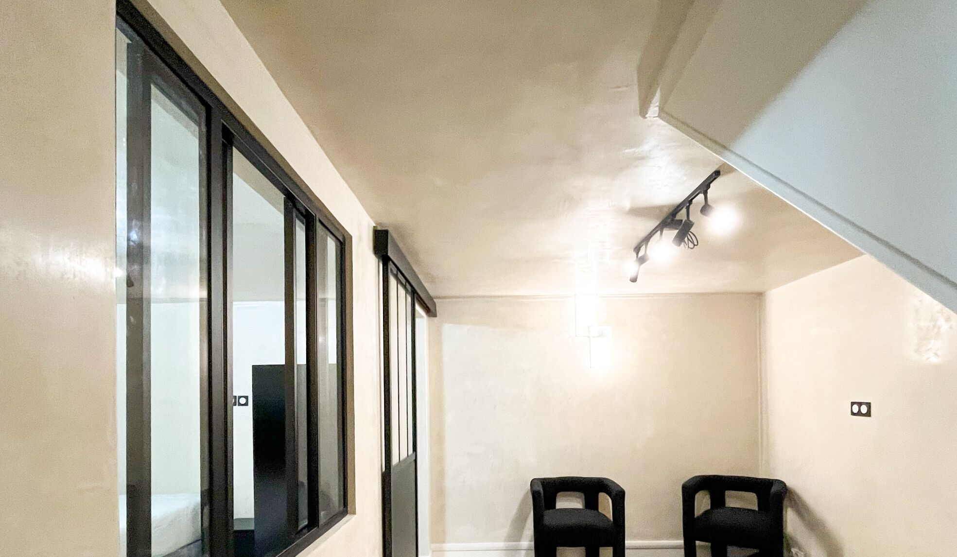 A small room with a large window, a ceiling light fixture, and two chairs.