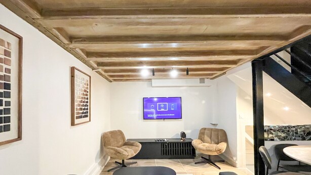 Una sala de estar moderna con techo de madera, un televisor montado, dos sillones y una mesa de comedor.