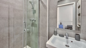 Un baño moderno con ducha de vidrio, un lavamanos blanco y un espejo encima.
