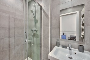 A modern bathroom with a glass-enclosed shower, a white sink, and a mirror above it.
