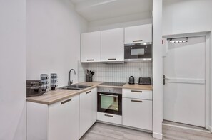 A compact kitchen with white cabinets, a built-in oven, a microwave, and a coffee maker.