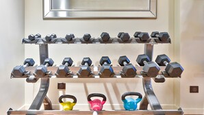 A wall-mounted dumbbell rack with multiple sets of hexagonal dumbbells and kettlebells.
