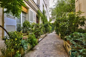A narrow cobblestone alley flanked by lush greenery and buildings with shutters.