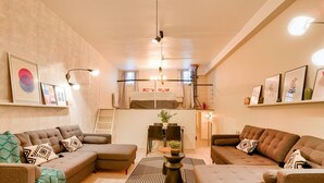 Un salon moderne comprenant un ensemble de canapés, une table à manger avec des chaises et un coin cuisine avec un lit en mezzanine.