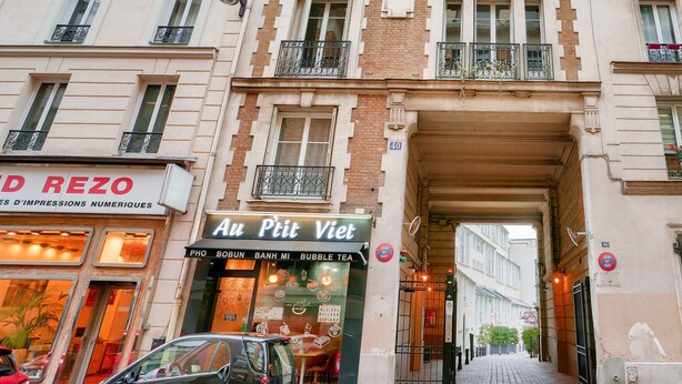 Une vue d’une rue, montrant un immeuble dont le rez-de-chaussée abrite un café appelé « Au P’tit Vêt ».