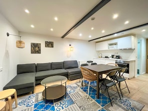 A modern living room with a sectional sofa, a dining table with chairs, a small coffee table, a kitchen area with white cabinets, and a patterned rug. - UrbanFlat 86 - Maison de ville au centre de Paris (París)