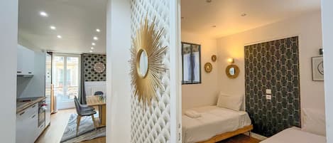 A modern room with a bed, a sofa, a dining area with a table and chairs, and a kitchen area.