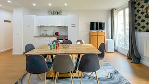 Una cucina moderna con mobili bianchi, un tavolo da pranzo in legno e un televisore su un mobile in legno.