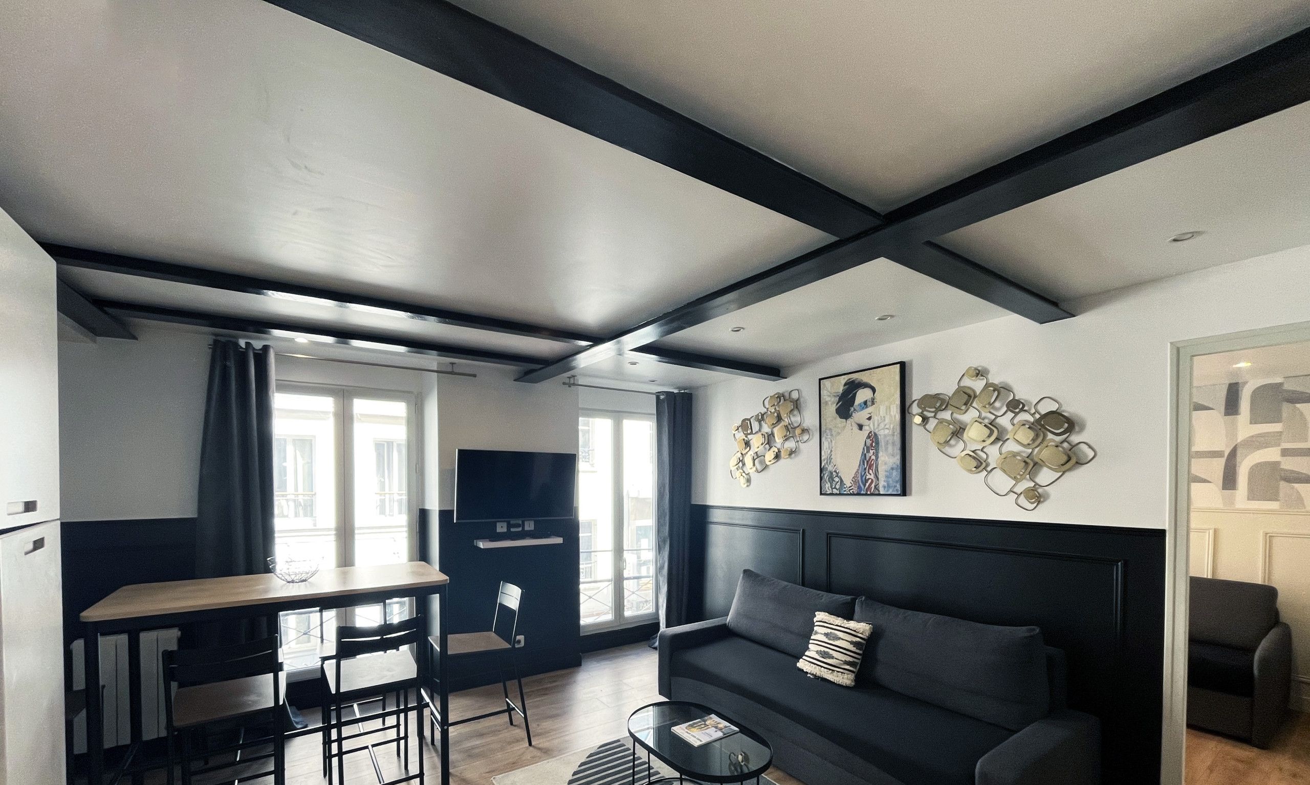 A modern living room with a dark sofa, a dining area with a table and chairs, and a kitchen area with a TV.