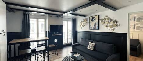 A modern living room with a dark sofa, a dining area with a table and chairs, and a kitchen area with a TV.