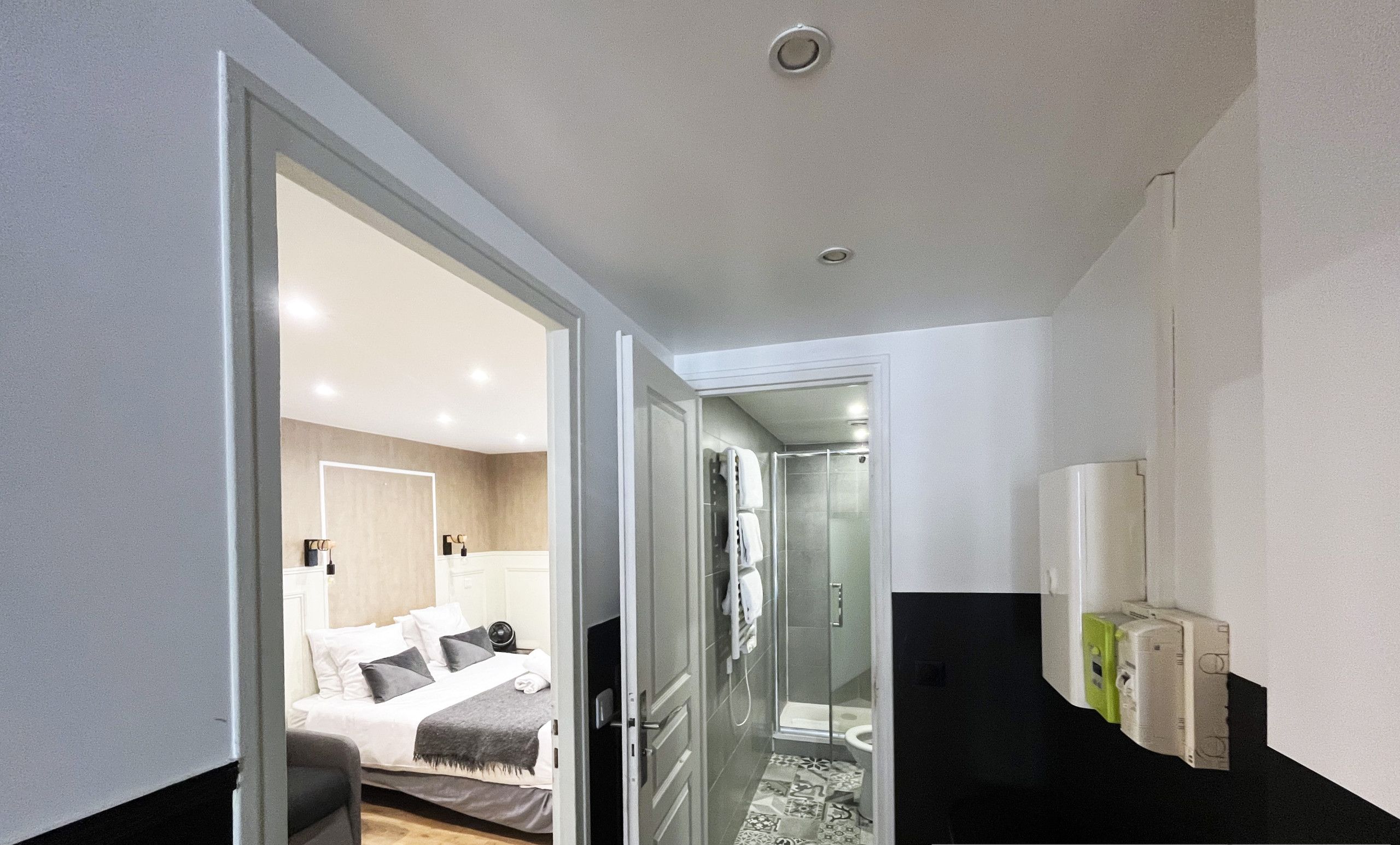 A modern hotel room with a bed, a shower, and a bathroom. There is a small rug on the floor and a towel hanging on the wall.