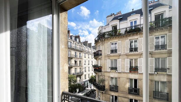 Une vue sur une rangée d’immeubles à plusieurs étages, dotés de balcons et de fenêtres, prise depuis une fenêtre.