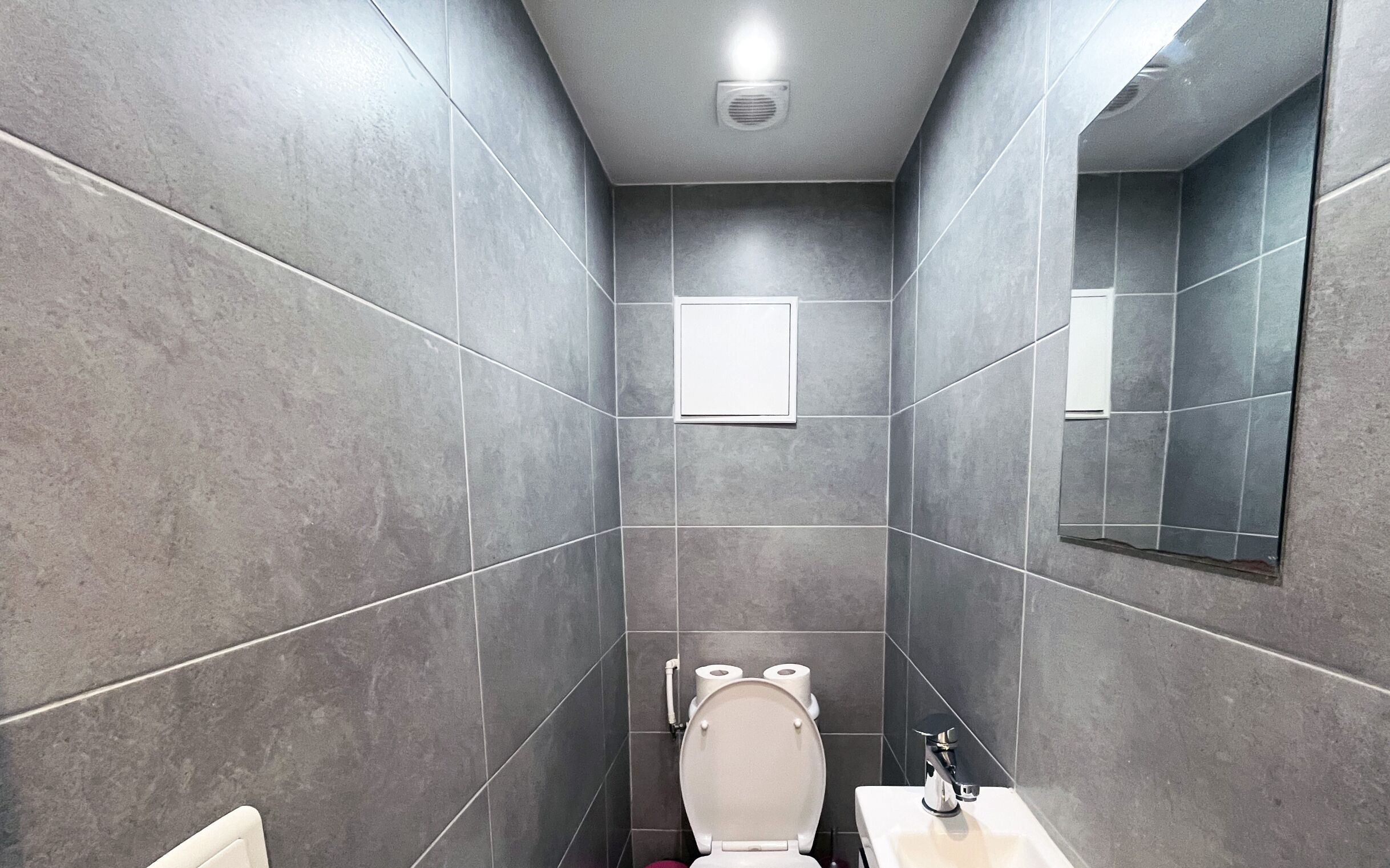 Une salle de bain moderne avec des carreaux gris, des toilettes, un lavabo et un miroir.